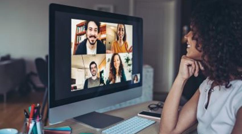 A woman smiles as she video calls a group of diverse colleagues from home.