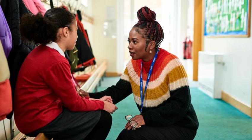 A teacher kneeling down talks to a student in the coatroom at school