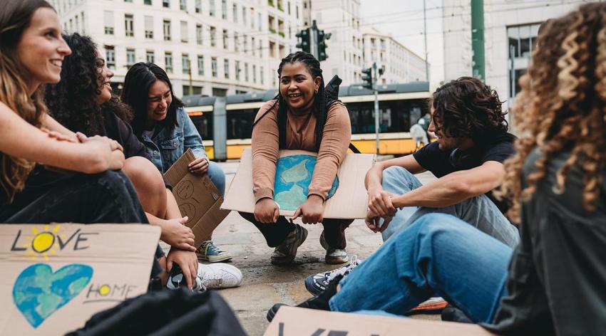 A group of students sit outdoors holding posters after an environmental justice protest.